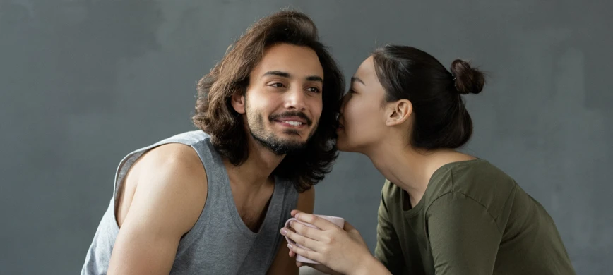 A woman whispering into her boyfriend's ear